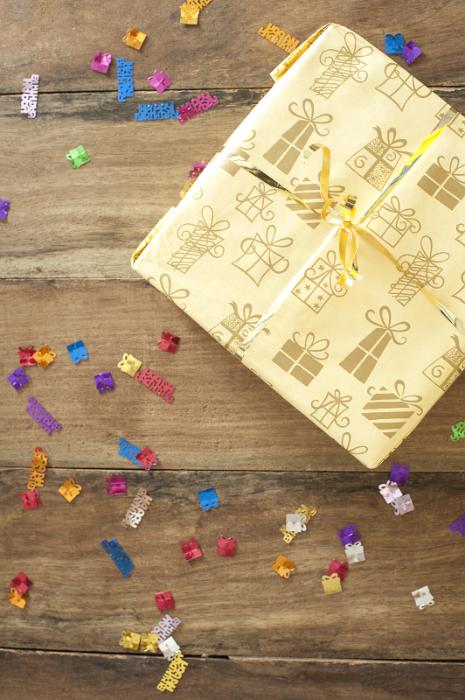 Free Stock Photo: Giftwrapped decorative birthday present with scattered colorful confetti on a wooden table at a birthday party