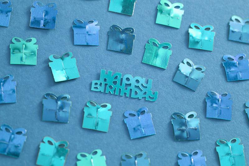 Free Stock Photo: Blue Metallic Happy Birthday Confetti Scattered on Blue Background, Shaped like Wrapped Presents with Birthday Message in Middle