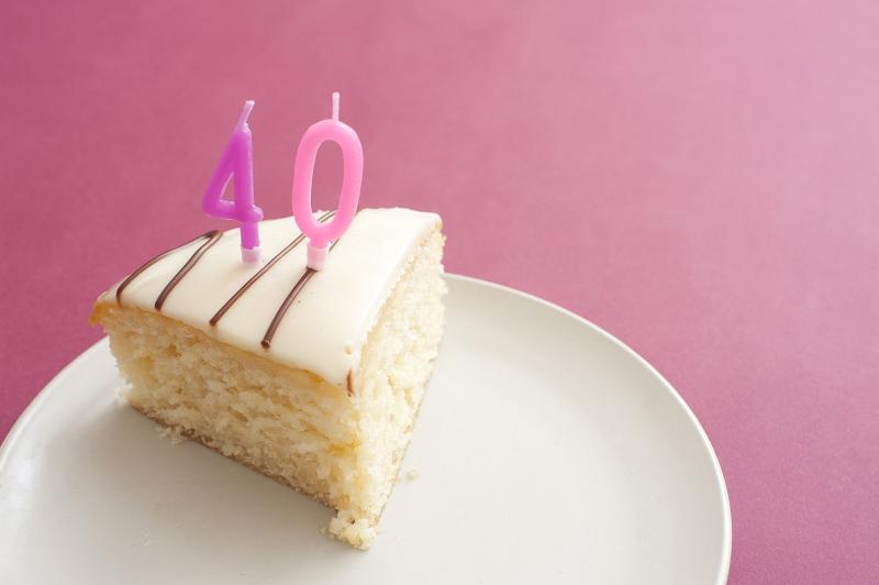 Free Stock Photo: Slice of cake with burning 40th birthday candles served on a plate over a pink background with copysace
