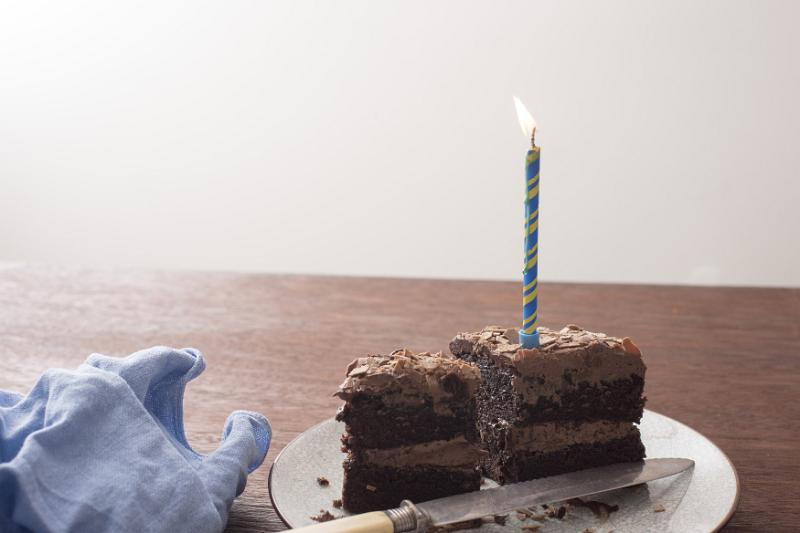 Free Stock Photo: Remnants of a tasty freshly baked chocolate birthday cake with single burning blue candle and knife on a table with napkin and copy space