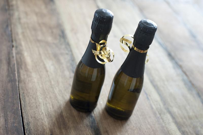 Free Stock Photo: Two small festive bottles of champagne tied with golden twirled ribbons standing side by side on a wooden table ready for a party or celebration, high angle view