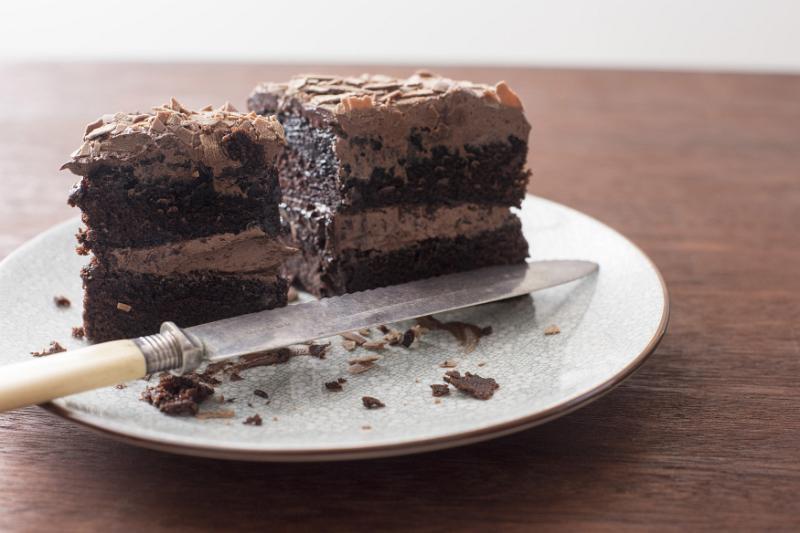 Free Stock Photo: Half eaten iced chocolate sponge cake with knife on a plate with crumbs over a wooden table