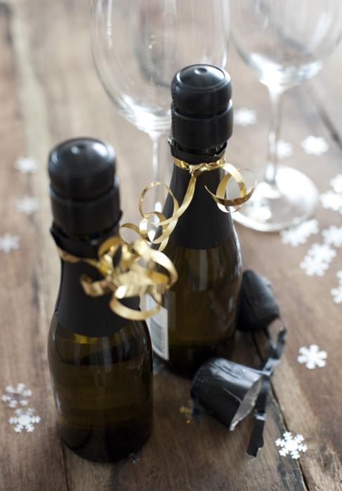 Free Stock Photo: Two Miniature Bottles of Champagne Tied with Gold Ribbon Surrounded by Glasses and Snowflake Confetti for Christmas or New Years Celebration