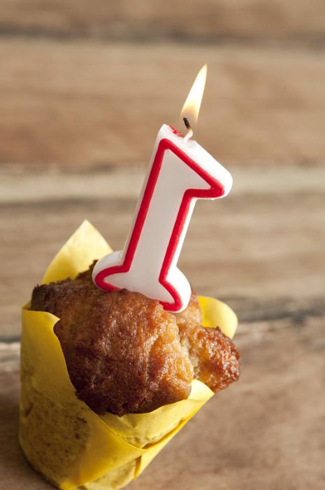 Free Stock Photo: Individual Cake or Muffin Wrapped in Yellow Paper with Burning Candle for First Birthday with Wooden Background