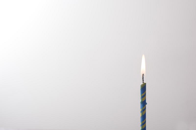 Free Stock Photo: Lone burning blue birthday candle placed to the side over a white background with copy space