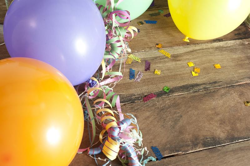 Free Stock Photo: Colorful Inflated Balloons Tied with Curled Ribbon Streamers Surrounded by Birthday Confetti with Copy Space on Wooden Background