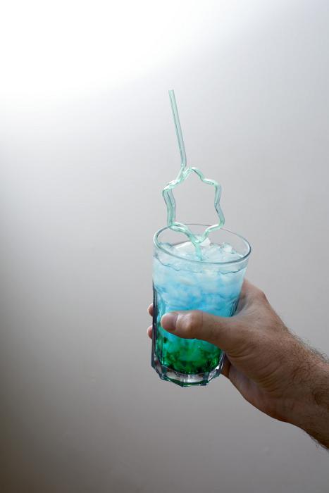 Free Stock Photo: Man holding a blue cocktail party drink with decorative bendy straw in a star shape over a grey background