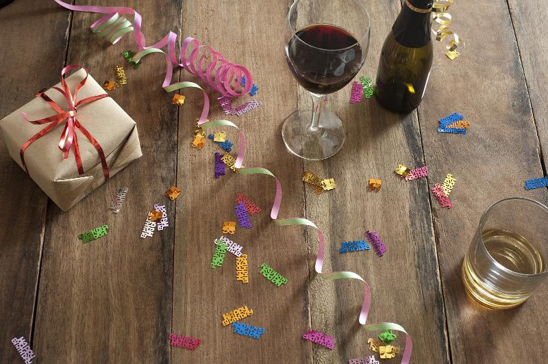 Free Stock Photo: Glasses and Bottle of Wine on Top of Wooden Table with Party Streamers, Confetti and Present in High Angle View.