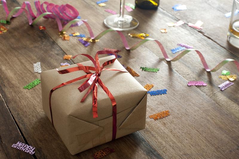 Free Stock Photo: Party gift with a decorative red ribbon bow lying on a wooden table with colorful streamers and confetti for a festive celebration