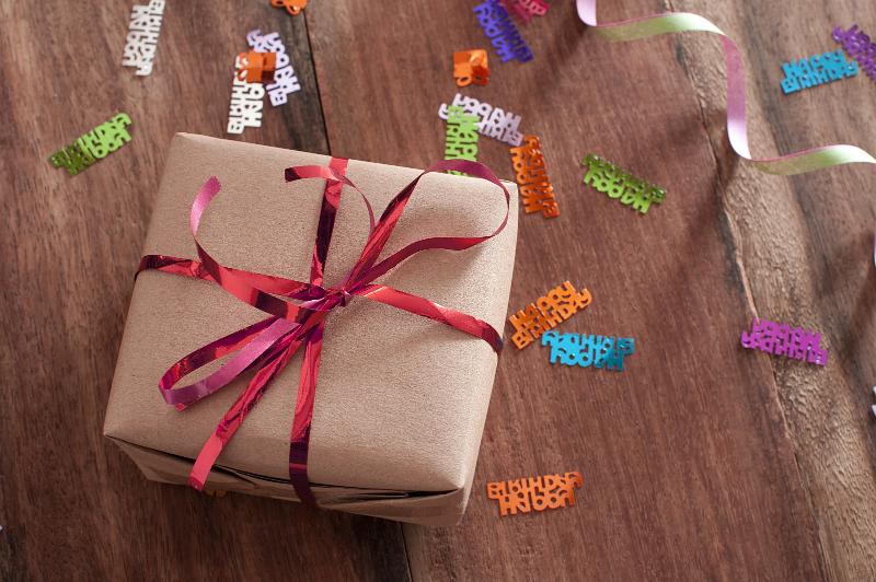 Free Stock Photo: Small gift on a wooden table with scattered confetti tied with a decorative red bow viewed high angle