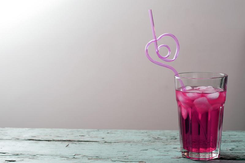 Free Stock Photo: Glass of red beverage with ice and curved heart shaped pink cocktail drinking straw on old wooden table. Copy space