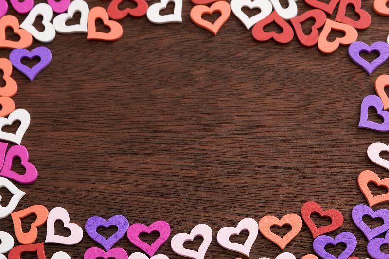 Free Stock Photo: Valentines Day heart frame on wood with colorful cut out heart shapes arranged as border over a textured wooden background with woodgrain and copy space