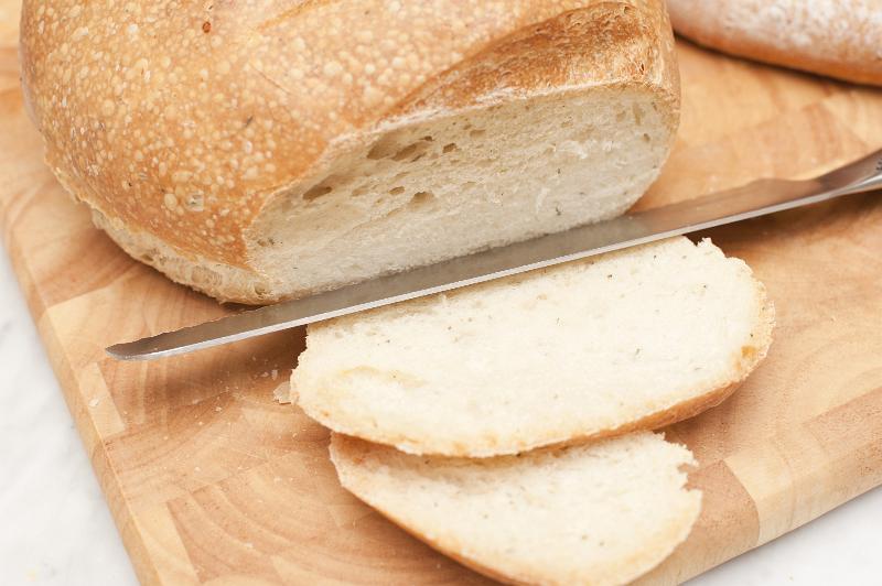 Free Stock Photo: Round loaf of fresh white bread with a knife and two cut slices on a wooden bread board