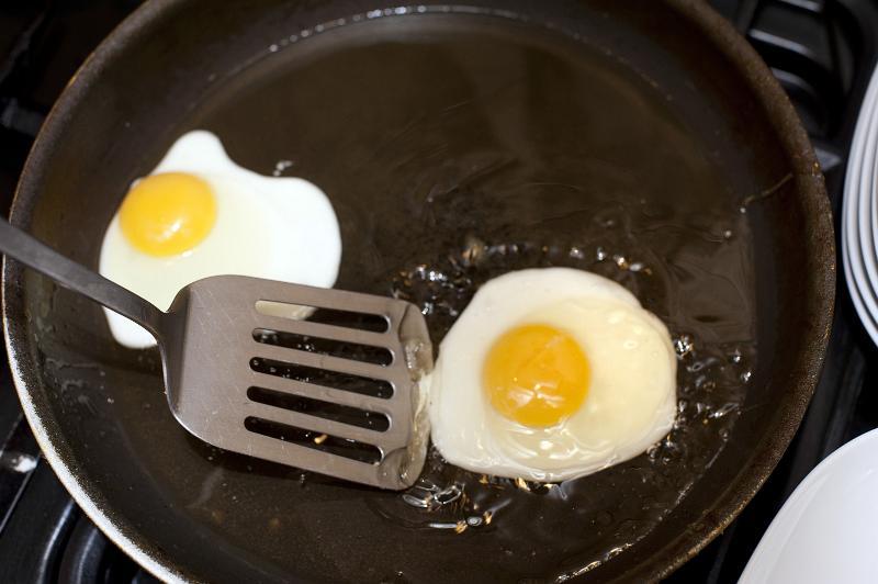 Free Stock Photo: Frying eggs for breakfast in a teflon coated frying pan in hot oil using a metal lifter kitchen utensil