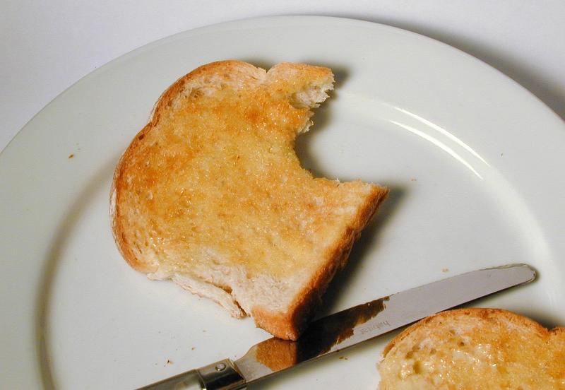 Free Stock Photo: Slice of hot buttered white toast on a white plate for breakfast bitten into on the corner
