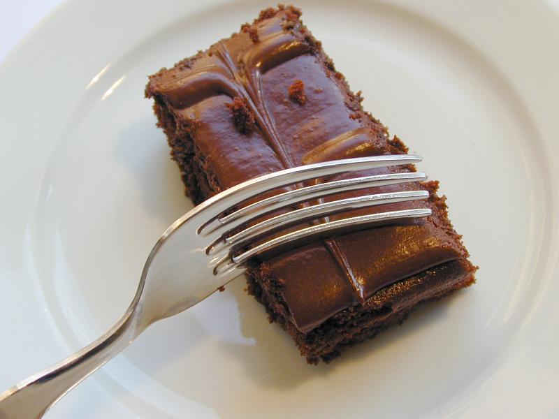 Free Stock Photo: Eating a portion of delcious chocolate cake topped with decorative icing with a fork, close up view on a white plate