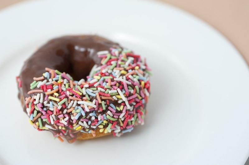 Free Stock Photo: Chocolate doughnut with one half decorated with colorful sprinkles served on a plate for a relaxing coffee break