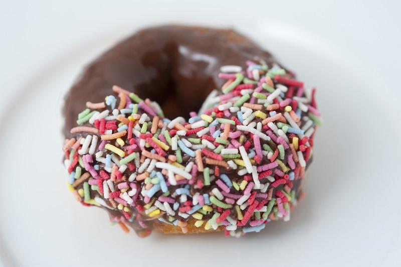 Free Stock Photo: Chocolate glazed ring donut dipped in colorful candy sprinkles on one side on a white plate with focus to the sprinkles