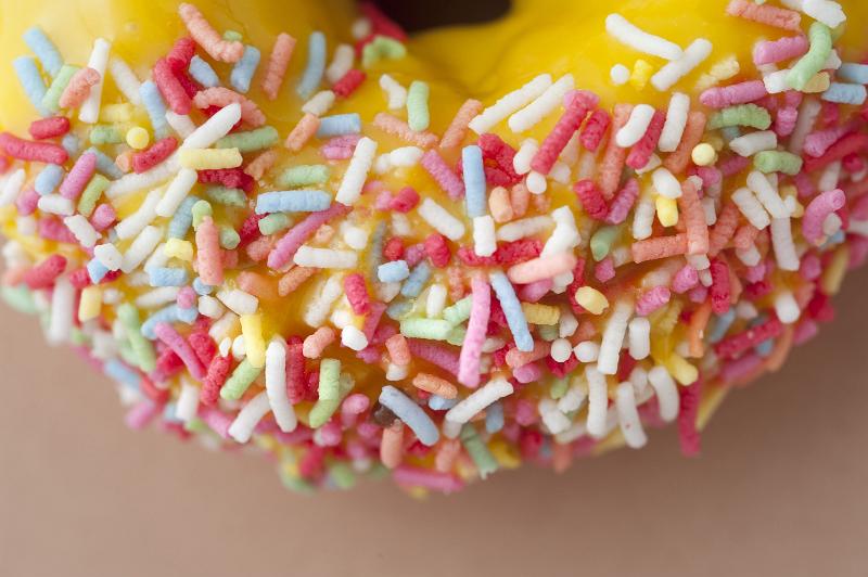 Free Stock Photo: Fresh doughnut with orange icing dipped in colorful sprinkles with a close up view of the sprinkles