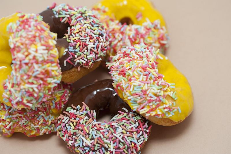 Free Stock Photo: Donut selection with chocolate and orange glazed ring doughnuts dipped in multicolored sprinkles piled on a white background