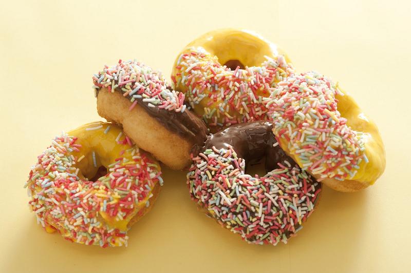Free Stock Photo: Pile of assorted fresh ring donuts or doughnuts glazed with chocolate, lemon or orange icing decorated with colorful sprinkles on a pale yellow background