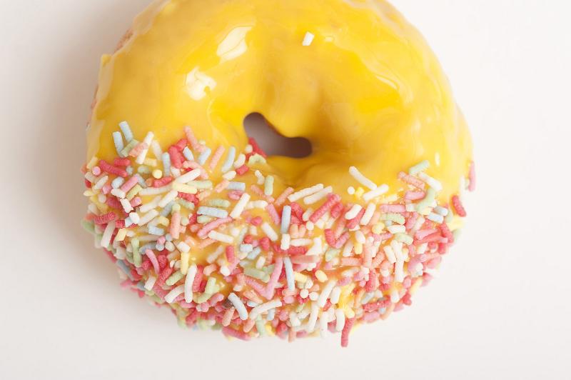 Free Stock Photo: Freshly baked glazed orange ring donut or doughnut decorated with multicolored sprinkles viewed from above on white
