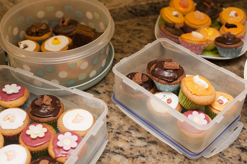Plastic containers of decorated mini cakes or cupcakes with colorfal assorted icing and butterflies and flowers ready for a childs birthday party