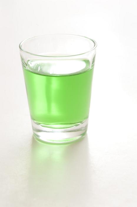 Free Stock Photo: Shot glass of green absinthe, a potent alcoholic spirit with a taste of anise, on a reflective white background with copyspace