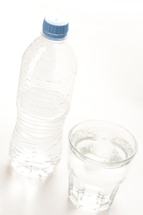 Free Stock Photo: Bottled water served in a glass tumbler with the half full capped unlabeled plastic bottle alongside, high angle tilted view
