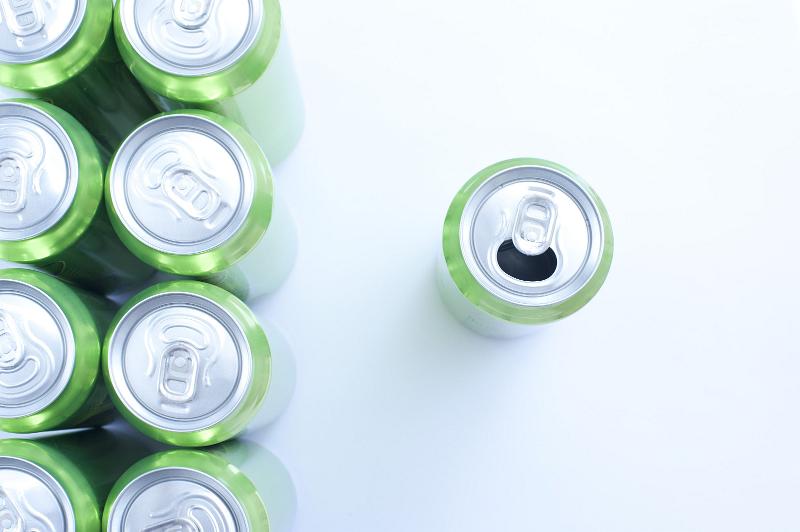 Free Stock Photo: Green aluminium drink cans neatly arranged in rows with a single can to the right that has been opened, overhead view on white with copyspace
