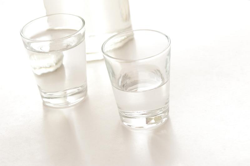 Free Stock Photo: Two shot glasses with servings of white spirits, possibly neat vodka, with the base of a bottle of alcohol in the background