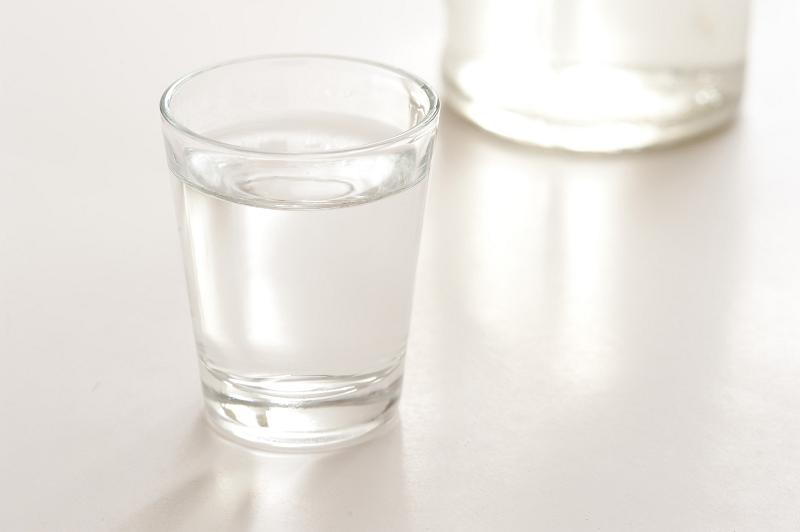 Free Stock Photo: Shot glass of clear pure vodka on a reflective white surface with the bottle of alcohol behind
