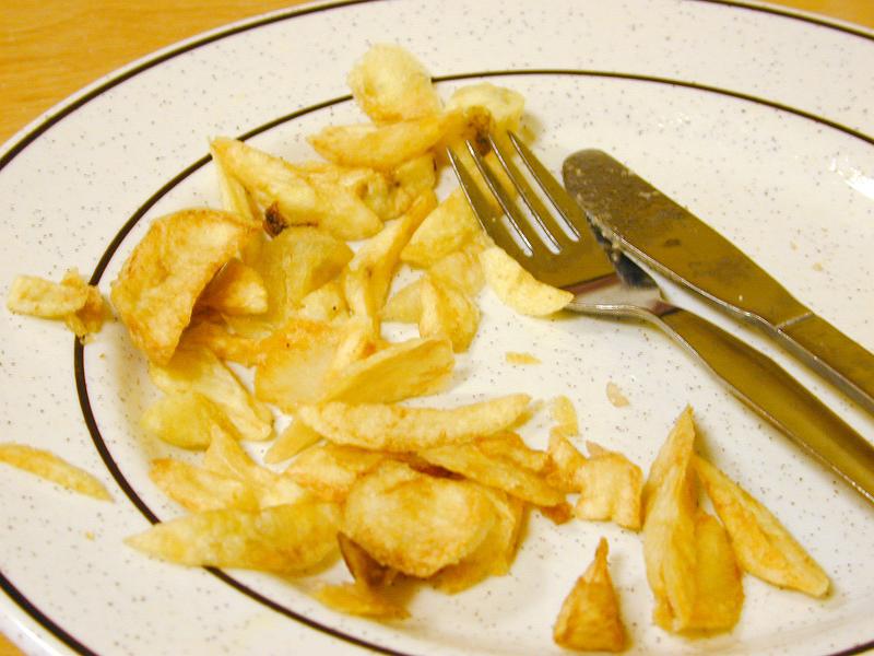 Free Stock Photo: Half eaten plate of golden deep fried potato chips on a plate with cutlery in a chip shop
