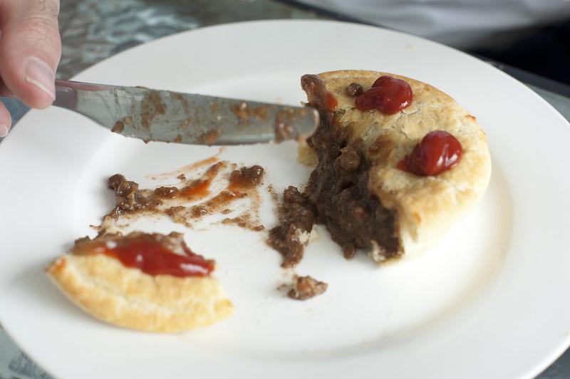 Free Stock Photo: Man eating a pastry meat pie topped with tomato ketchup cutting it with a knife, close up view