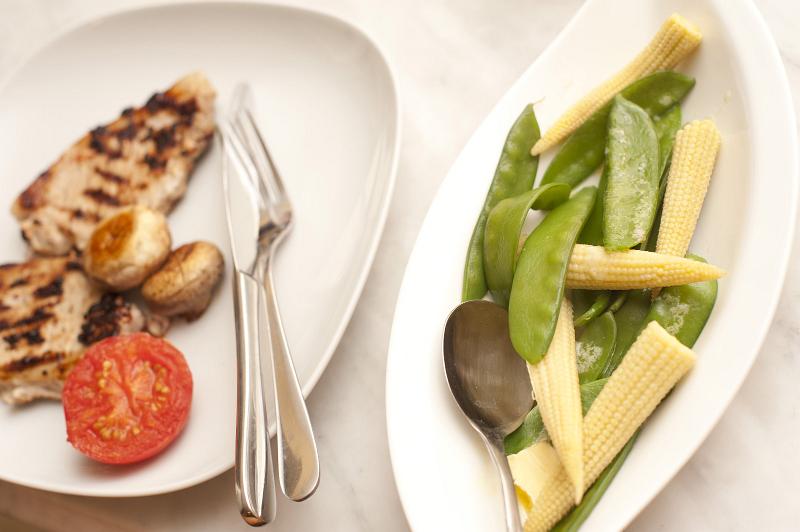 Free Stock Photo: Serving of two lean grilled pork chops with mushrooms and tomato and a side dish of vegetables containing mangetout or sugar snap peas and baby corn on the cob