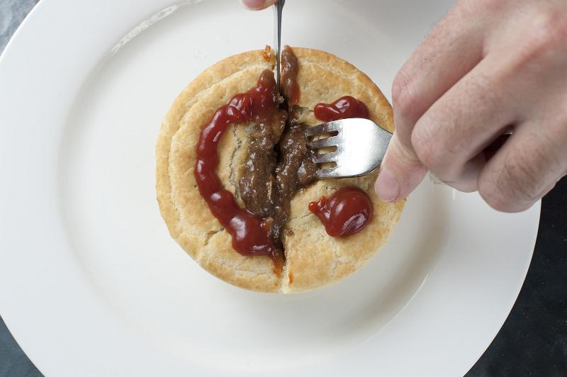 Free Stock Photo: Man cutting open a tasty meat pie with a cute gravy face on top of the pastry using a knife and fork as he prepares to eat it for lunch, high angle close up view