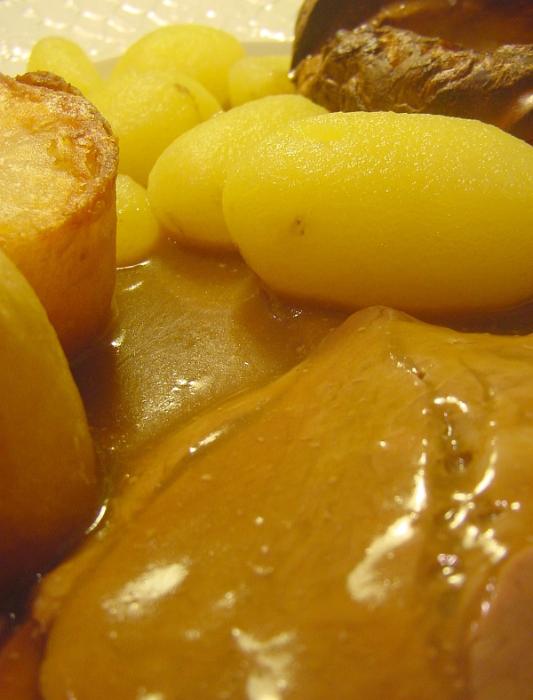 Free Stock Photo: Roast beef dinner with a close up view of a slice of beef covered in rich gravy served with roast potatoes and Yorkshire pudding