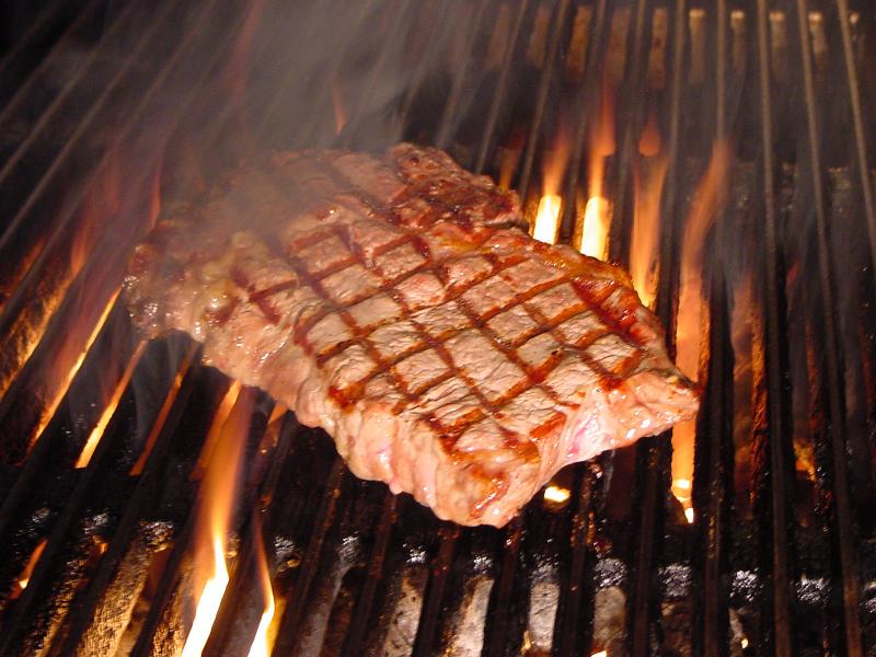 Free Stock Photo: Grilling a tasty tender beef steak on the barbecue over the hot flames on a metal grid at an outdoor summer picnic, close up view