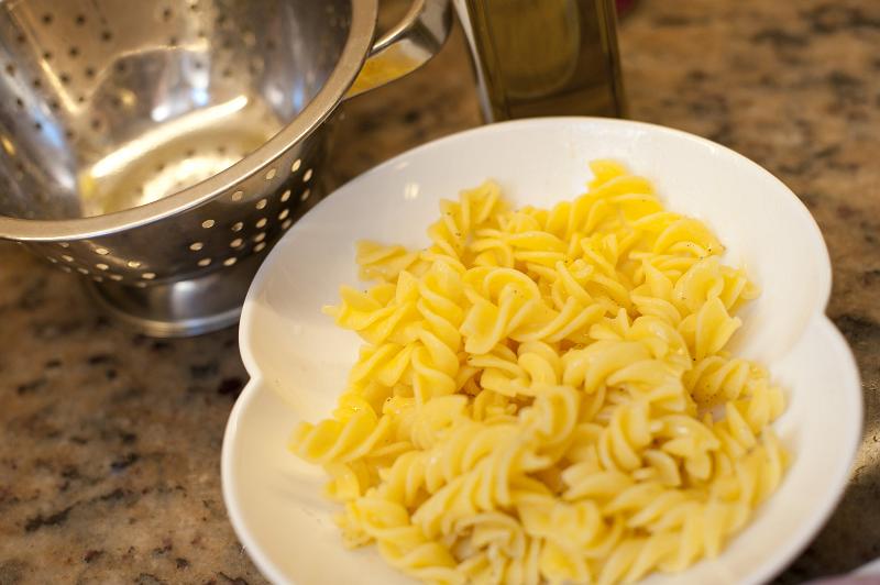 Free Stock Photo: Plate of plain cooked Italian spiral pasta standing on a kitchen counter alongside a metal colander for draining it