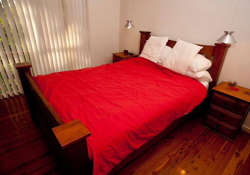 Free Stock Photo: Bedroom interior decor with an old fashioned wooden bed with a red cover with hanging lamps on either side and a window with a closed floor length blind