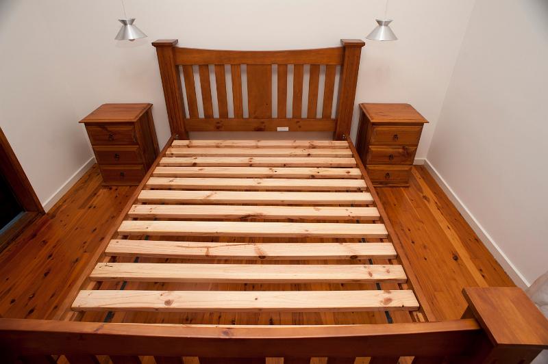 Free Stock Photo: Wooden slatted bed frame with no mattress and two matching bedside tables in a small bedroom