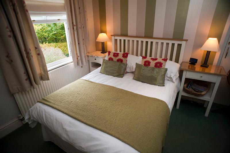 Free Stock Photo: Homely bedroom interior with a double bed and lighted lamps on bedside tables alongside a window with a garden view and striped wallpaper