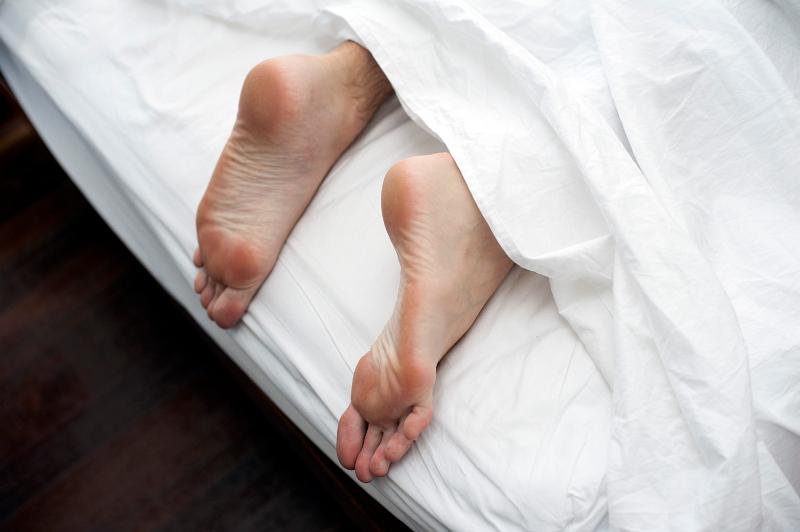 Free Stock Photo: Man lying in bed on a lazy day with his feet sticking out the bottom of the bed from under the white bedclothes, close up view