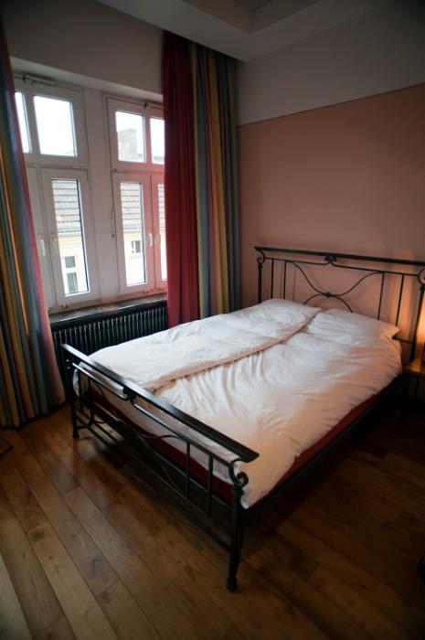 Free Stock Photo: Metal frame double bed in an austere bedroom interior with a bare wooden floor and high windows overlooking an urban building