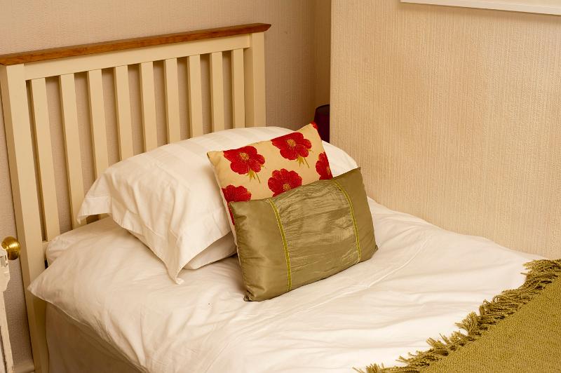 Free Stock Photo: Single bed with white bed linen and decorative gold and red cushions with a simple wooden headboard, closeup view