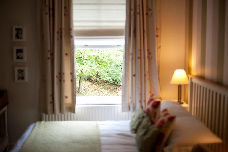 Free Stock Photo: Homely bedroom with a double bed and window looking out over a leafy green garden illuminated by a bedside lamp