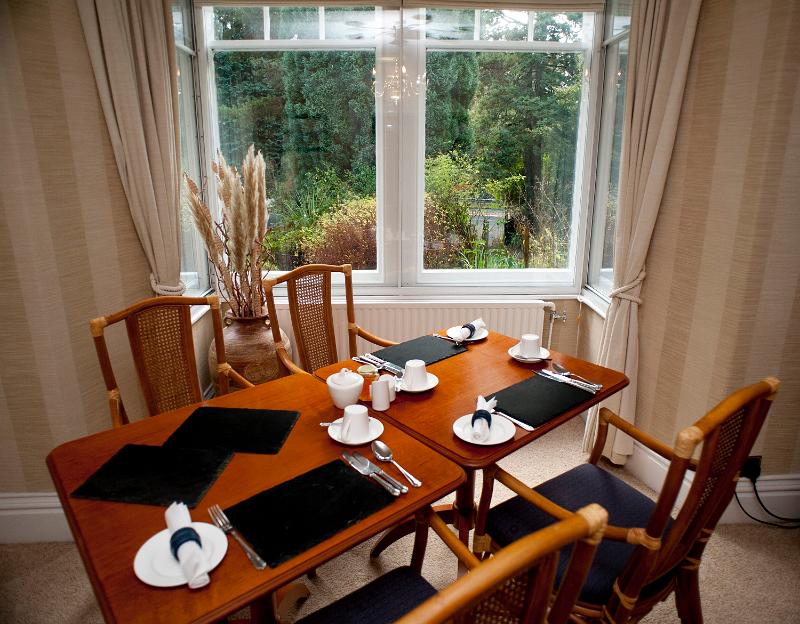 Free Stock Photo: Stylish wooden dining table set for three people for breakfast with cutlery and crockery alongside a view window overlooking shrubs