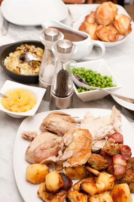 Free Stock Photo: Family dinner laid out on a dining table with a platter of carved roast meat, roast potatoes, peas, vegetables and gravy for a wholesome meal