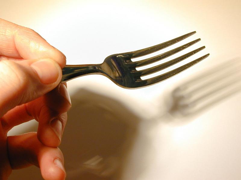 Free Stock Photo: Close up of the fingers of a man holding a fork casting a shadow onto a white plate