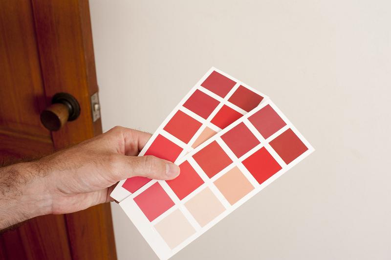 Free Stock Photo: Man holding two cards of colorful red paint swatches to a wall, close up view of his hand in a renovations, interior decorating or DIY concept